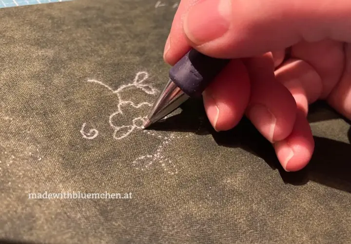 Ein Stift überträgt ein zartes Blumenmuster als Stickmuster auf Stoff.