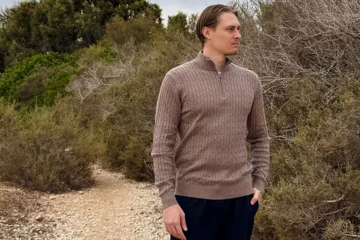 Mann in braunem Zopfmuster-Pullover aus Kaschmir, der in der Natur steht. Ist Kaschmir warm? Ja, dieser Pullover beweist es.