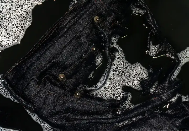Eine schwarze Hose wird gewaschen. Schaum und Wasser bedecken den Stoff, der gerade gereinigt wird.