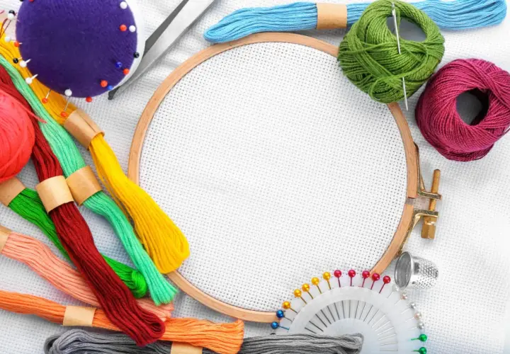 Buntes Stickgarn, Nadeln, Schere, Fingerhut und Stickrahmen – alles, was man zum Sticken braucht, liegt bereit für kreative Projekte.