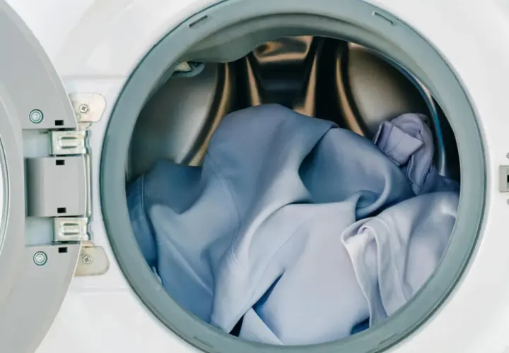Blaue Kleidung, darunter ein Hemd aus Polyester, wartet im Trommel der Waschmaschine auf den Schleudergang.