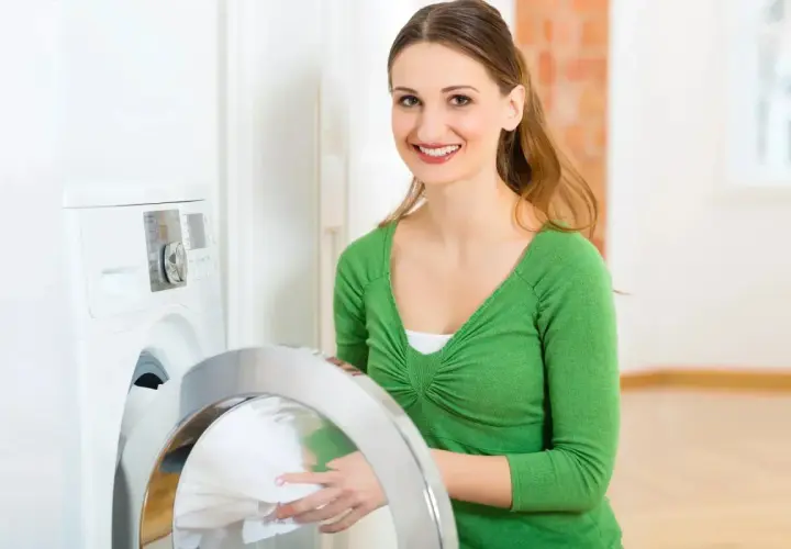 Lächelnde Frau lädt Wäsche in die Waschmaschine. Sie wählt das passende mix programm für ihre Kleidung.