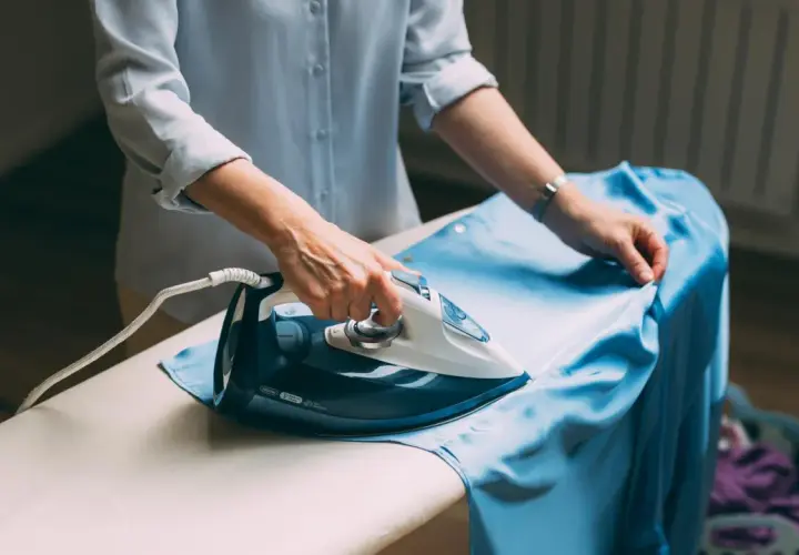 Frau bügelt ein hellblaues Kleid aus knitterfreier Viskose.