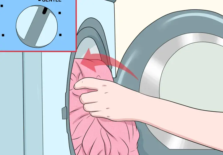 Hand lädt ein rosa Kleid in die Waschmaschine. Das Programm "Sanft" ist eingestellt, um zu verhindern, dass die Viskose eingelaufen ist.