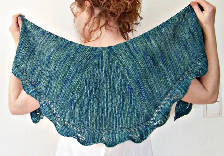 Frau hält ein wunderschönes, blau-grün meliertes **Tuch stricken** mit zarten Lochmustern am Rand.