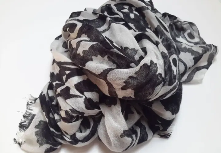 Ein leicht zerknitterter Schal aus Polyester-Plastik mit einem auffälligen schwarz-weißen Blumenmuster.