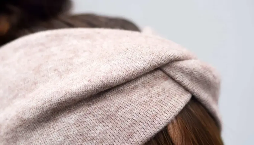 Ein gestricktes Stirnband in Beige mit einem Knoten vorne. Die Breite des Stirnbands ist ideal für einen gemütlichen Look.