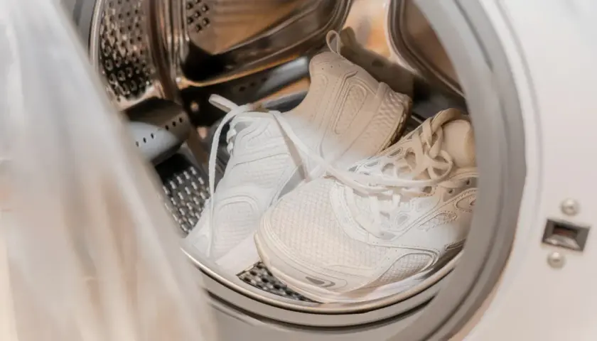 Weiße Sportschuhe in der Trommel einer Waschmaschine, bereit für das Waschprogramm Sport.