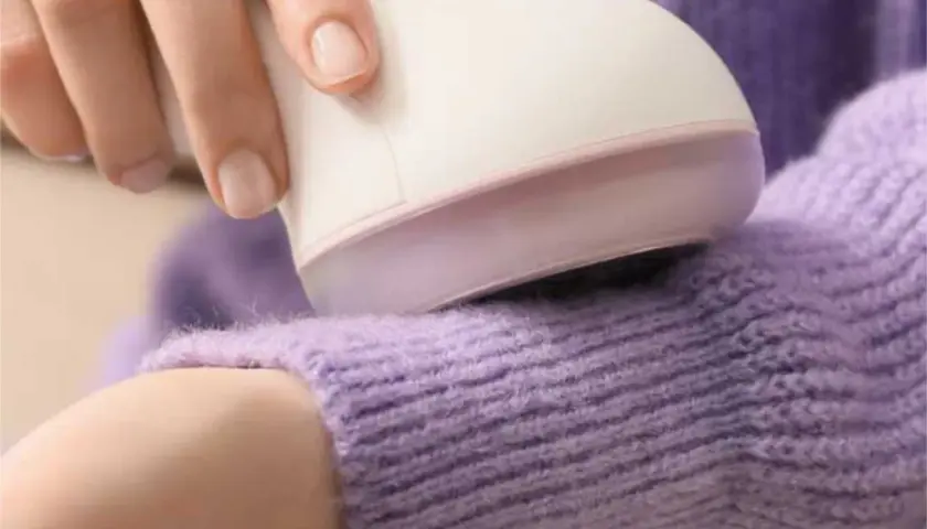 Hand uses a device to remove pilling from a lavender sweater.