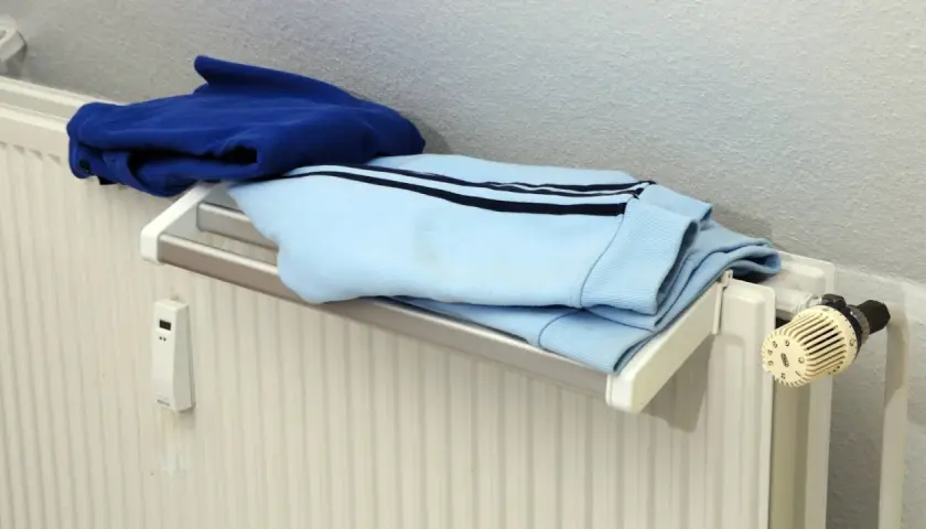 Blaue und hellblaue Kleidung trocknet auf einem Heizkörper. Ein kleiner weißer Kasten mit Display hängt an der Wand.