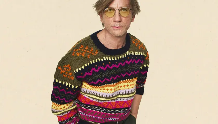 Mann mit gelber Brille trägt bunten wollpullover. Er fragt sich, wie er diesen am besten waschen kann, um die Farben zu erhalten.