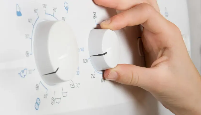 Hand dreht am Regler der Waschmaschine, um einen Kurzprogramm zu wählen.