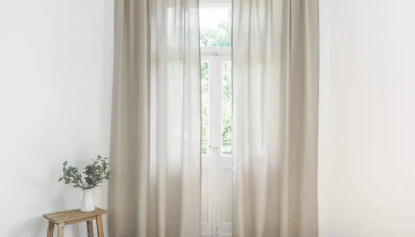 Helle Leinen Gardinen hängen vor einem Fenster. Sie sind frisch gewaschen und duften nach Sommer.