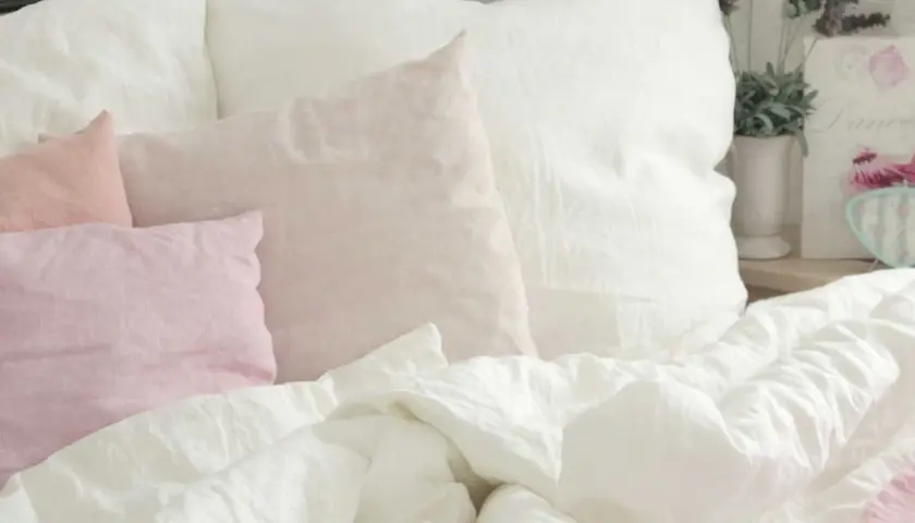 Ein Bett mit weißen und rosafarbenen Leinenkissen. Das Leinen kratzt sanft, lädt zum Entspannen ein.