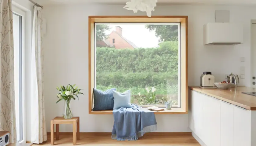 Ein Fensterplatz mit Kissen und Decke lädt zum Verweilen ein. Die Gardinenstange ist dezent gehalten, um den Blick nach draußen nicht zu stören.