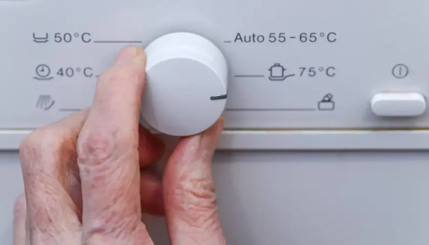 Hand dreht Regler an Waschmaschine. Das 30 Grad Programm ist nicht sichtbar, aber 40°C und 50°C sind wählbar.