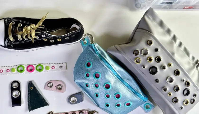 Schwarzer Sneaker mit goldenen Schnürsenkeln, blaue und graue Taschen mit vielen Ösen. Material für Ösen-Kleidung.