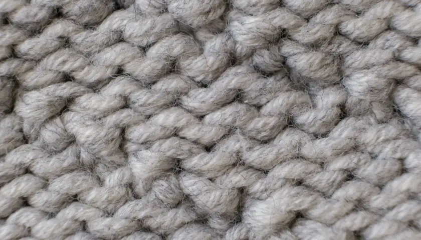 Nahaufnahme einer dicken, grauen Stricktextur. Die Garnstränge sind grob und flauschig, perfekt für einen gemütlichen **Wolle trockner**.