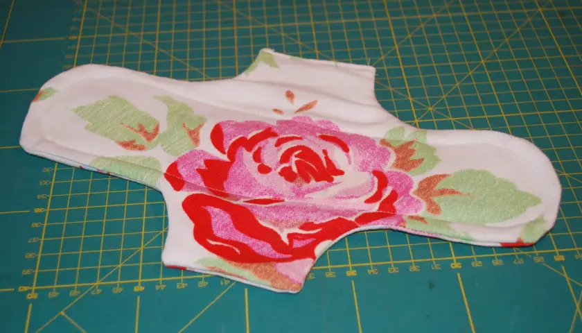 Eine selbstgenähte Stoffbinde mit Blumenmuster liegt auf einer Schneidematte. Das Nähen von Stoffbinden ist eine nachhaltige Alternative.