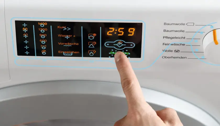 Finger drückt auf Start/Stop an Waschmaschine. Display zeigt 2:59. Wähle das richtige Programm für Wolle, achte auf die richtige Temperatur.