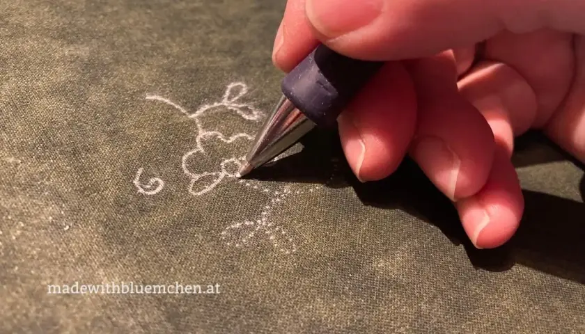 Ein Stift überträgt ein zartes Blumenmuster als Stickmuster auf Stoff.