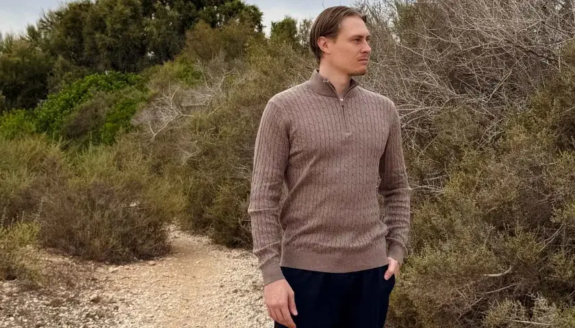 Mann in braunem Zopfmuster-Pullover aus Kaschmir, der in der Natur steht. Ist Kaschmir warm? Ja, dieser Pullover beweist es.
