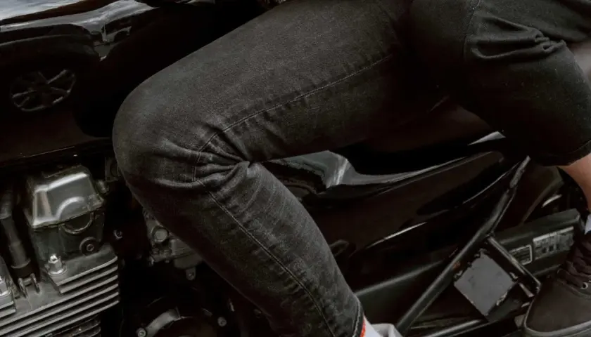 Person sitzt auf einem Motorrad, trägt schwarze Jeans, die frisch gewaschen aussehen, und Motorradhandschuhe.