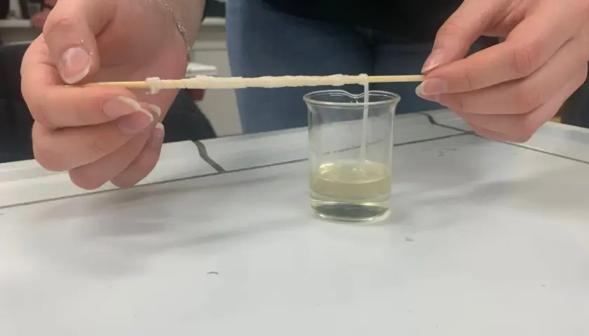 Hände ziehen einen Faden aus einer Flüssigkeit, der zeigt, woraus Nylon besteht.