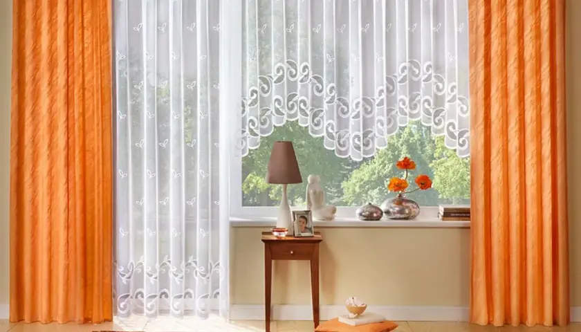 Orange und weiße Gardinen formen ein gemütliches Fensterbild. Zarte Muster zieren die weißen Stoffe, während die orangefarbenen Vorhänge Wärme ausstrahlen.