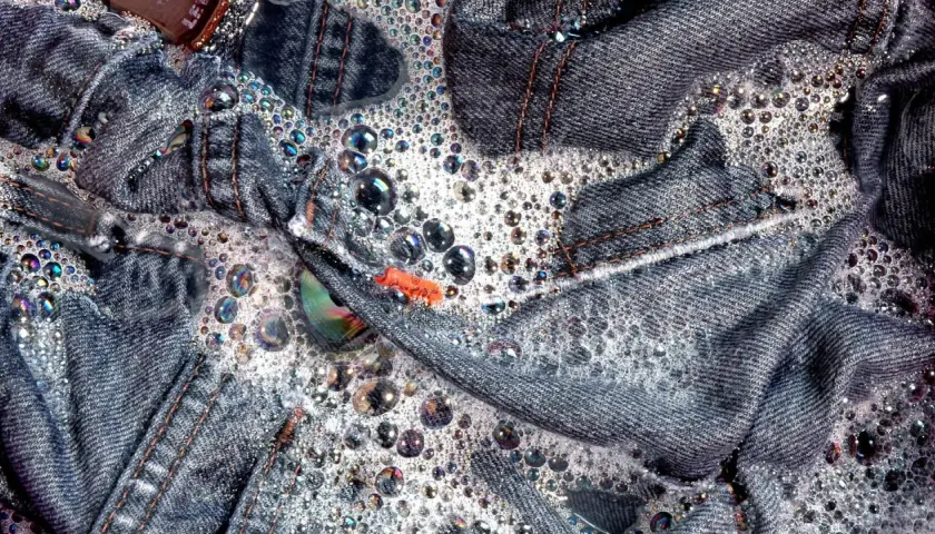 Jeans schleudern in schaumigem Wasser. Bunte Seifenblasen tanzen auf dem Denim.