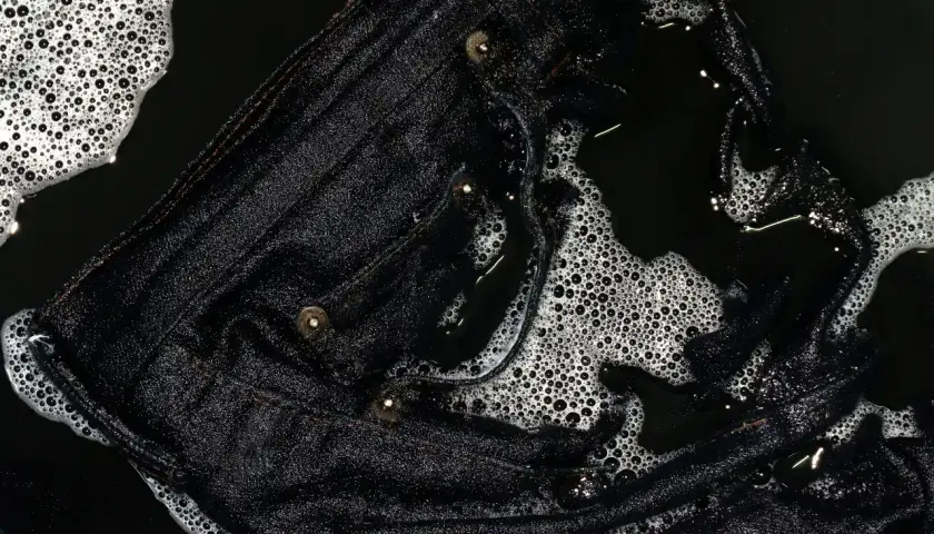 Eine schwarze Hose wird gewaschen. Schaum und Wasser bedecken den Stoff, der gerade gereinigt wird.
