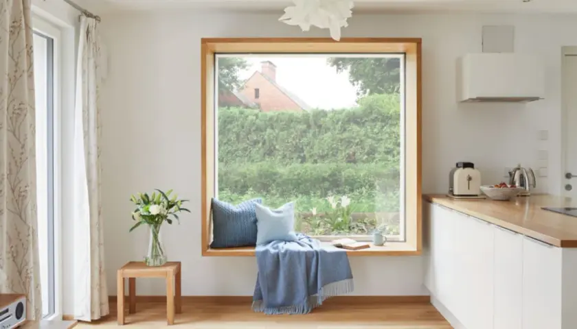 Gemütliche Sitzecke am Fenster ohne Fensterbank: Kissen, Decke und Buch laden zum Verweilen ein.