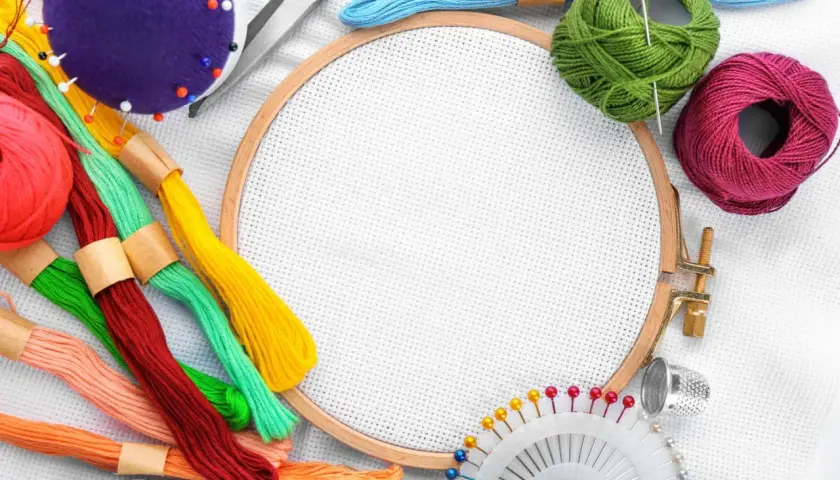 Buntes Stickgarn, Nadeln, Schere, Fingerhut und Stickrahmen – alles, was man zum Sticken braucht, liegt bereit für kreative Projekte.