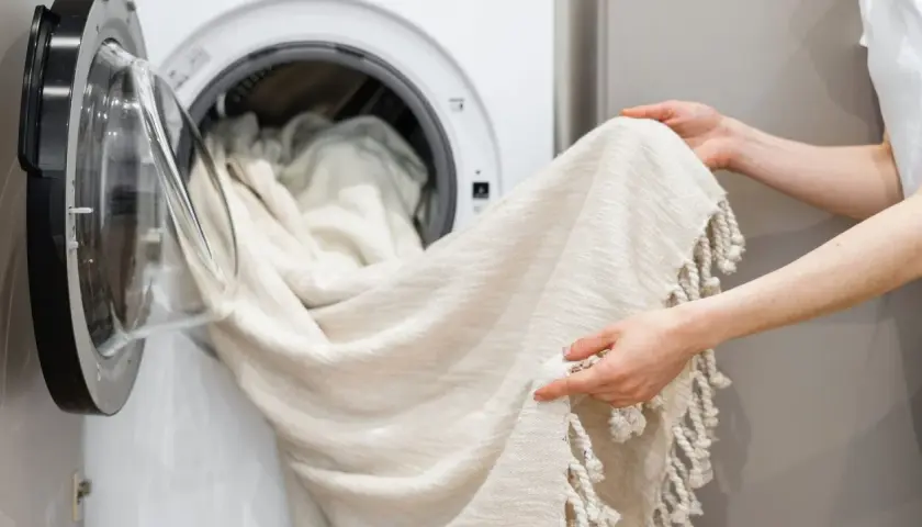 Helle Gardinen werden in die Waschmaschine geladen. Ein Hausmittel wie Backpulver kann helfen, sie wieder strahlend weiß zu machen.