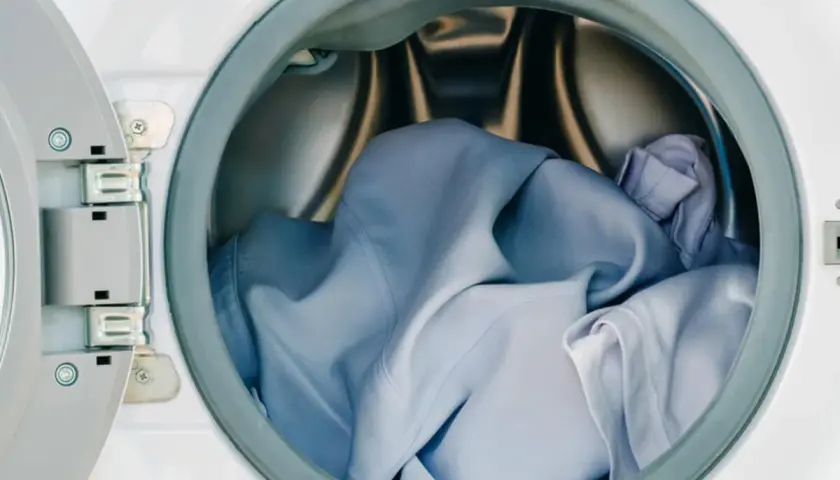 Blaue Kleidung, darunter ein Hemd aus Polyester, wartet im Trommel der Waschmaschine auf den Schleudergang.