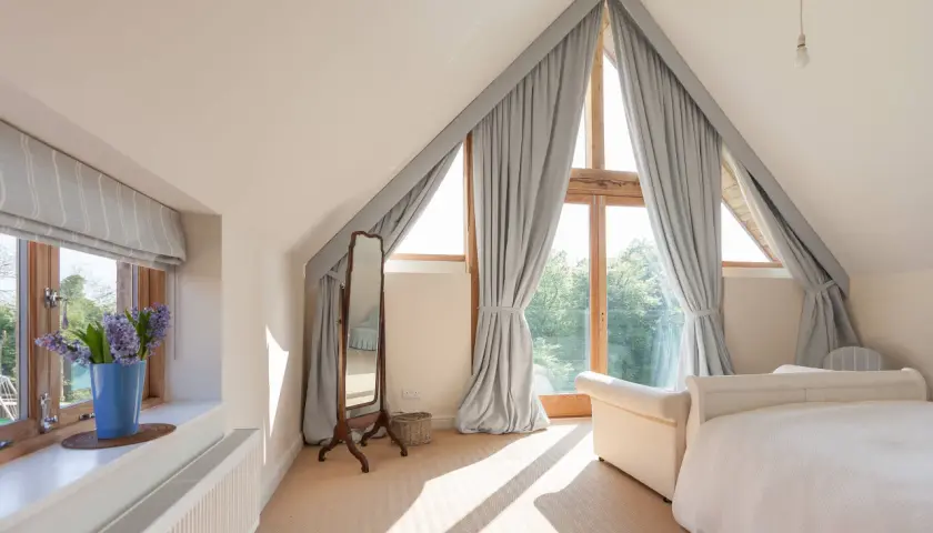 Graue Vorhänge rahmen ein Dreiecksfenster ein und lassen viel Licht herein. Sie sind elegant mit Bändern befestigt.
