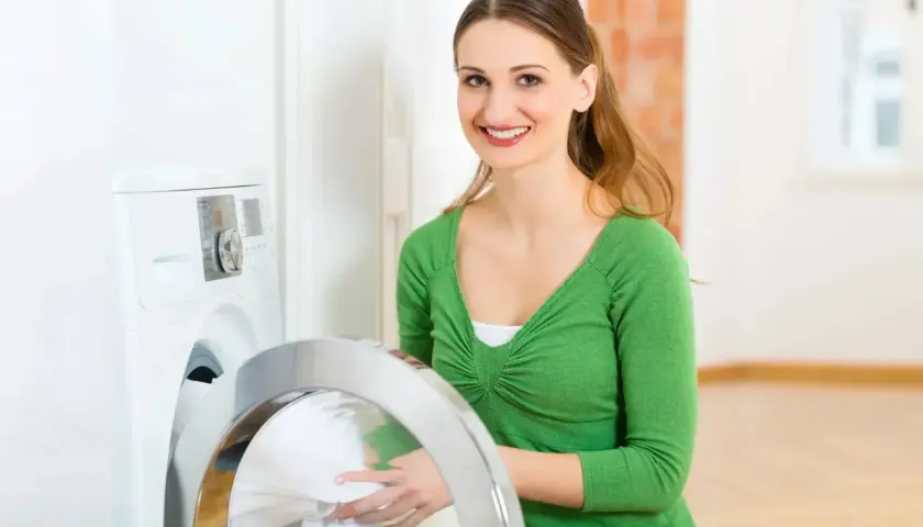 Lächelnde Frau lädt Wäsche in die Waschmaschine. Sie wählt das passende mix programm für ihre Kleidung.