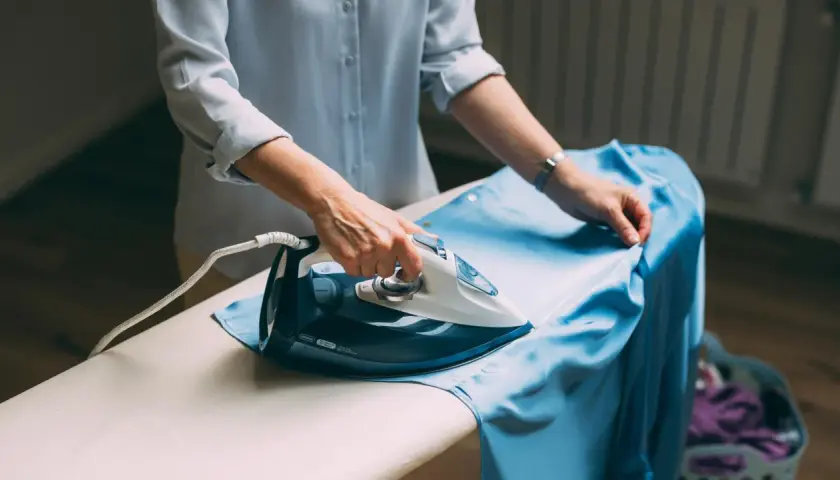 Frau bügelt ein hellblaues Kleid aus knitterfreier Viskose.