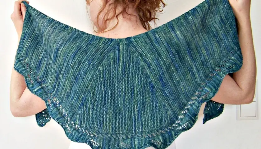 Frau hält ein wunderschönes, blau-grün meliertes **Tuch stricken** mit zarten Lochmustern am Rand.