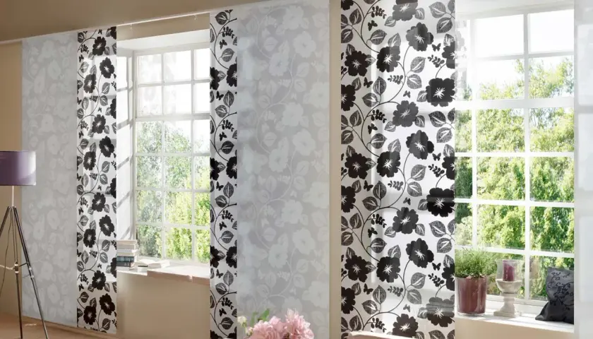 Schiebegardine kurz mit floralem Muster in Schwarz und Weiß. Helle Paneele mit zarten Blüten und dunklere mit kräftigen Blumen und Schmetterlingen schmücken das Fenster.