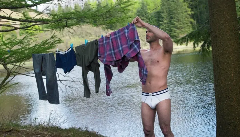 Mann hängt Wäsche auf, darunter auch eine **Boxershorts**, zum Trocknen am Seeufer.