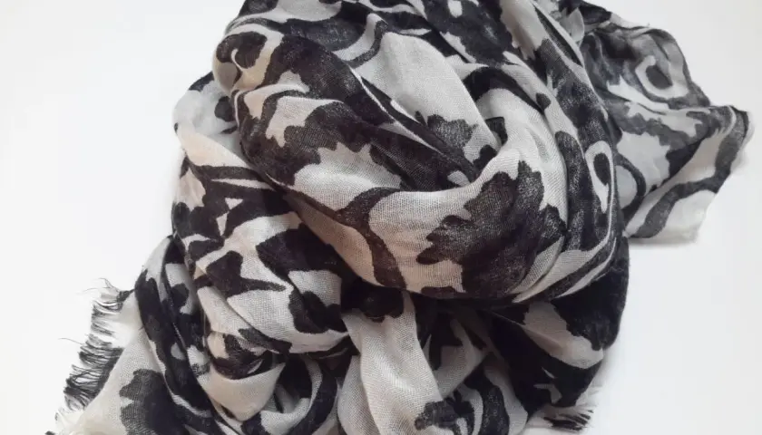 Ein leicht zerknitterter Schal aus Polyester-Plastik mit einem auffälligen schwarz-weißen Blumenmuster.