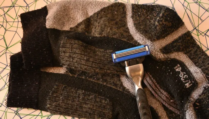 Rasierklinge liegt auf einem stark verknöteltem, gemustertem Schlauch. Pilling hose wird mit der Klinge entfernt.