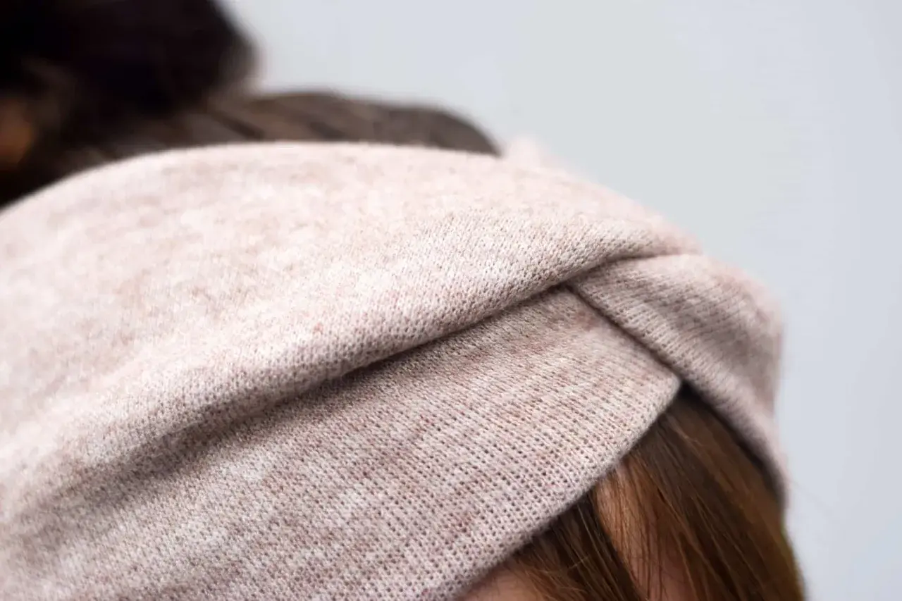 Ein gestricktes Stirnband in Beige mit einem Knoten vorne. Die Breite des Stirnbands ist ideal für einen gemütlichen Look.