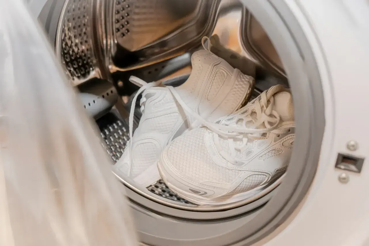 Weiße Sportschuhe in der Trommel einer Waschmaschine, bereit für das Waschprogramm Sport.