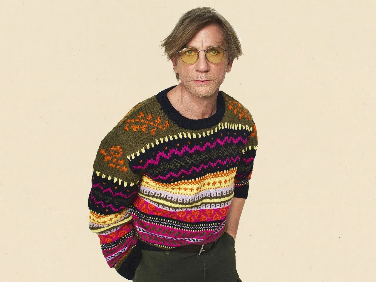 Mann mit gelber Brille trägt bunten wollpullover. Er fragt sich, wie er diesen am besten waschen kann, um die Farben zu erhalten.