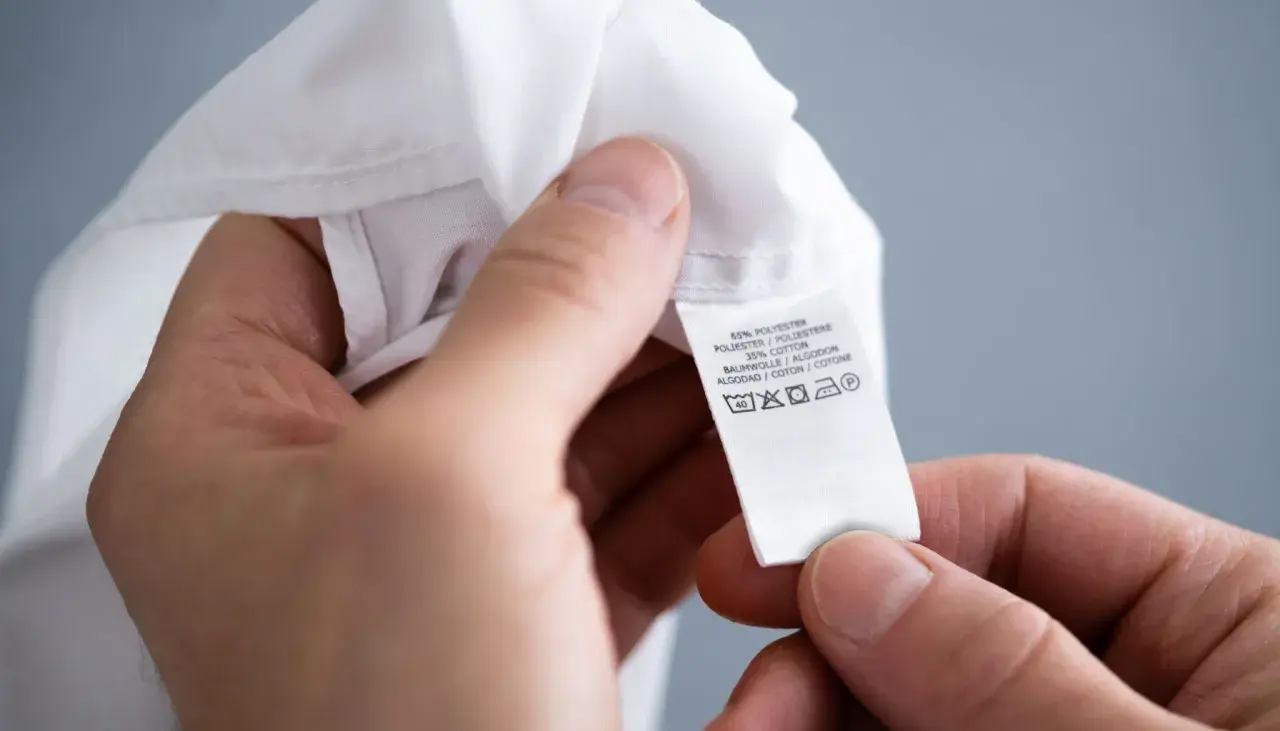 Ein Etikett zeigt Pflegehinweise für ein Kleidungsstück aus Polyester und Baumwolle, inklusive Symbol für einen synthetik waschgang bei 40 Grad.