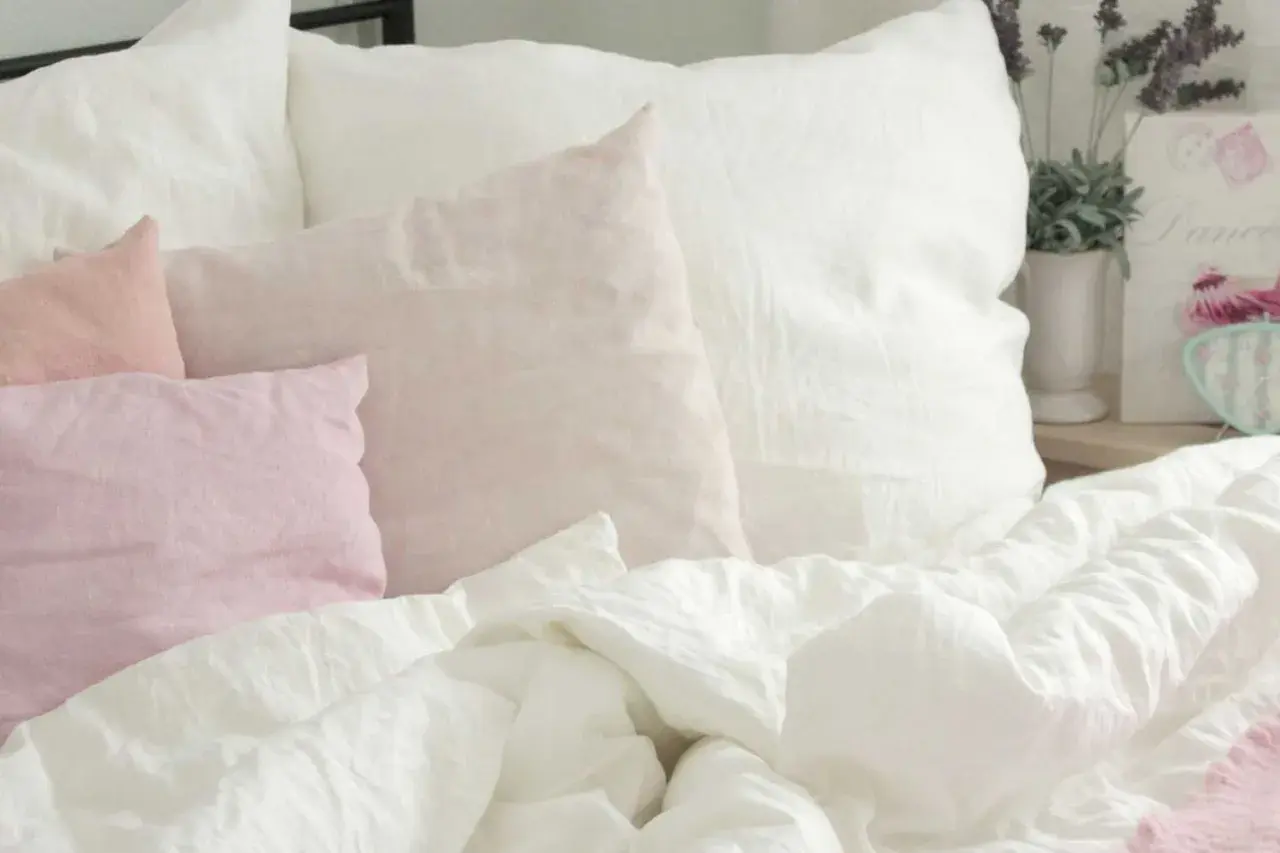 Ein Bett mit weißen und rosafarbenen Leinenkissen. Das Leinen kratzt sanft, lädt zum Entspannen ein.