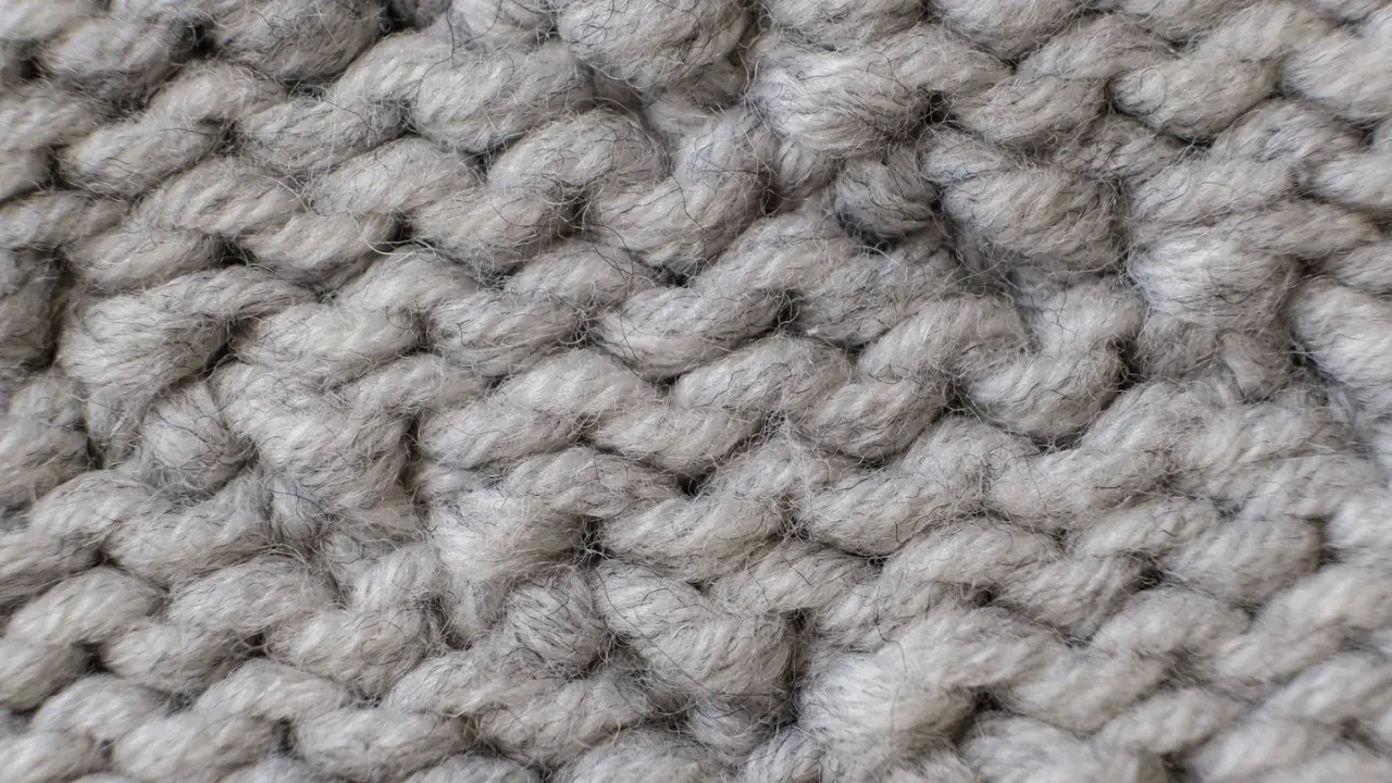 Nahaufnahme einer dicken, grauen Stricktextur. Die Garnstränge sind grob und flauschig, perfekt für einen gemütlichen **Wolle trockner**.