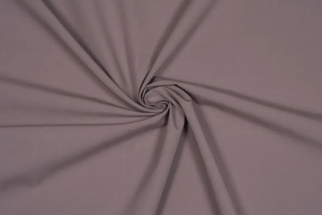 Ein glatter, taupefarbener Stoff, der sich zu einer Spirale dreht. Dies ist ein Beispiel für Popeline, ein dicht gewebtes Baumwollmaterial.